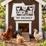 A decorative metal chicken coop sign reading 'THE CHICK-INN EST. 2025 NO VACANCY' mounted on a brown coop, with several chickens standing and walking around it in a garden setting.