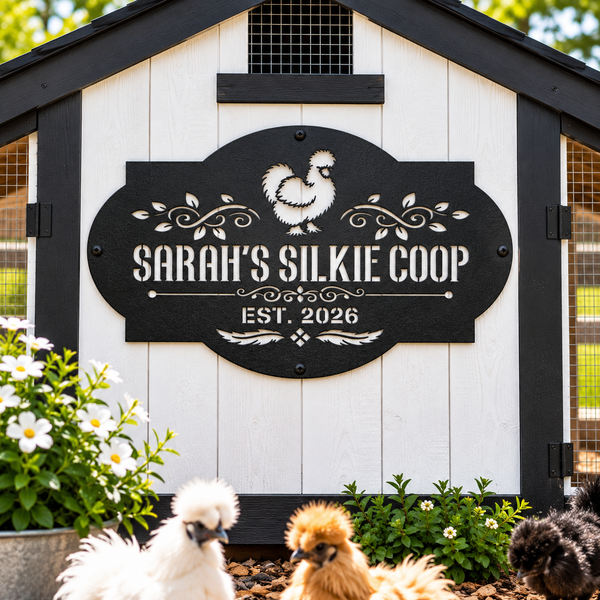 A decorative black metal sign with white lettering reading 'SARAH'S SILKIE COOP' and 'EST. 2026,' mounted on a white chicken coop.