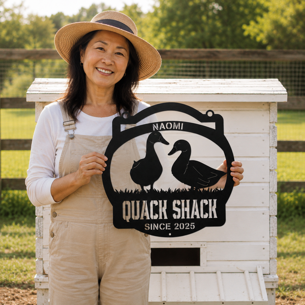 A smiling woman in a straw hat and beige overalls stands outdoors in front of a white wooden coop, holding a black metal sign that reads 'NAOMI QUACK SHACK SINCE 2025' with duck silhouettes.