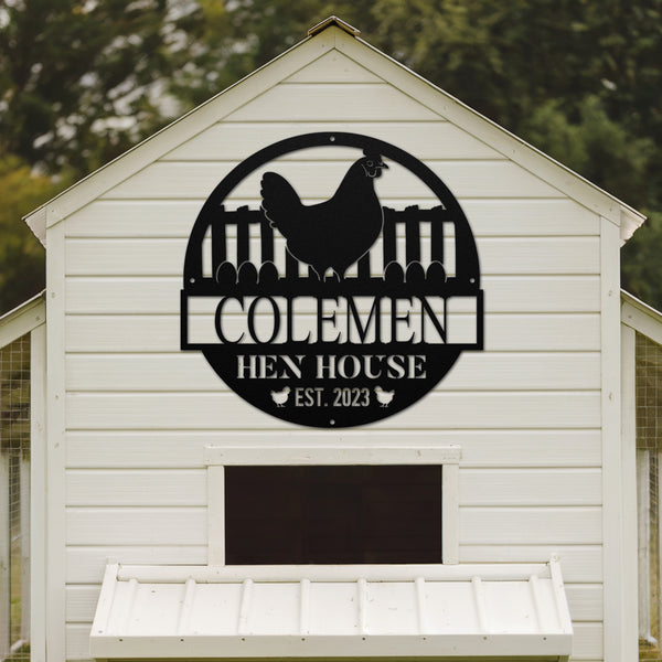 White chicken coop with a black metal sign featuring a rooster and 'COLEMAN HEN HOUSE EST. 2023' text.
