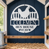A white metal sign reading “COLEМЕН HEN HOUSE EST. 2023” with a chicken silhouette and fence cutout, mounted on a dark blue wooden chicken coop wall above a wooden perch.