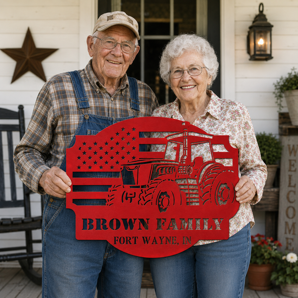An elderly couple stands on a front porch holding a large red decorative sign shaped like a tractor over an American flag, with the text 'BROWN FAMILY' and 'FORT WAYNE, IN'.