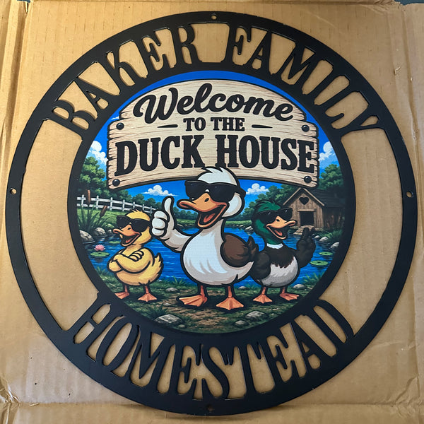 A circular metal sign for the 'Baker Family Homestead' featuring cartoon ducks at 'Welcome to the Duck House' on a cardboard backing.
