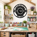 A styled craft room interior with a wooden workbench, shelves of supplies, plants, and a large circular wall sign reading 'She Shed' with decorative text. The scene is clearly a real environment rather than a clean isolated product shot, so subject_type is Lifestyle.