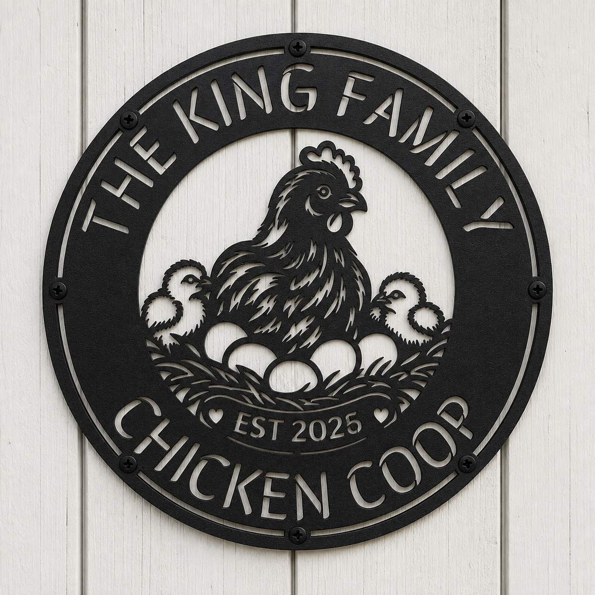 A round black metal sign mounted on a white wood plank wall, featuring a cutout design of a hen with three chicks and eggs, with the text 'THE KING FAMILY CHICKEN COOP' and 'EST 2025'.