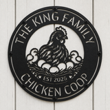 A round black metal sign mounted on a white wood plank wall, featuring a cutout design of a hen with three chicks and eggs, with the text 'THE KING FAMILY CHICKEN COOP' and 'EST 2025'.