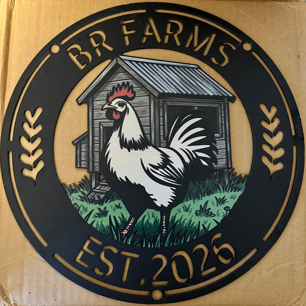 A circular metal sign for 'BR FARMS' featuring a graphic illustration of a white and black rooster standing in front of a gray wooden barn with green grass. The sign has a black background with gold-colored text reading 'BR FARMS' at the top and 'EST.