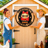Two women standing on a chicken coop door holding a large circular black metal sign that reads 'CHRISTINE'S CHICKEN COOP' with a cartoon chick wearing glasses and a red bow. Chickens are visible at the bottom of the scene.