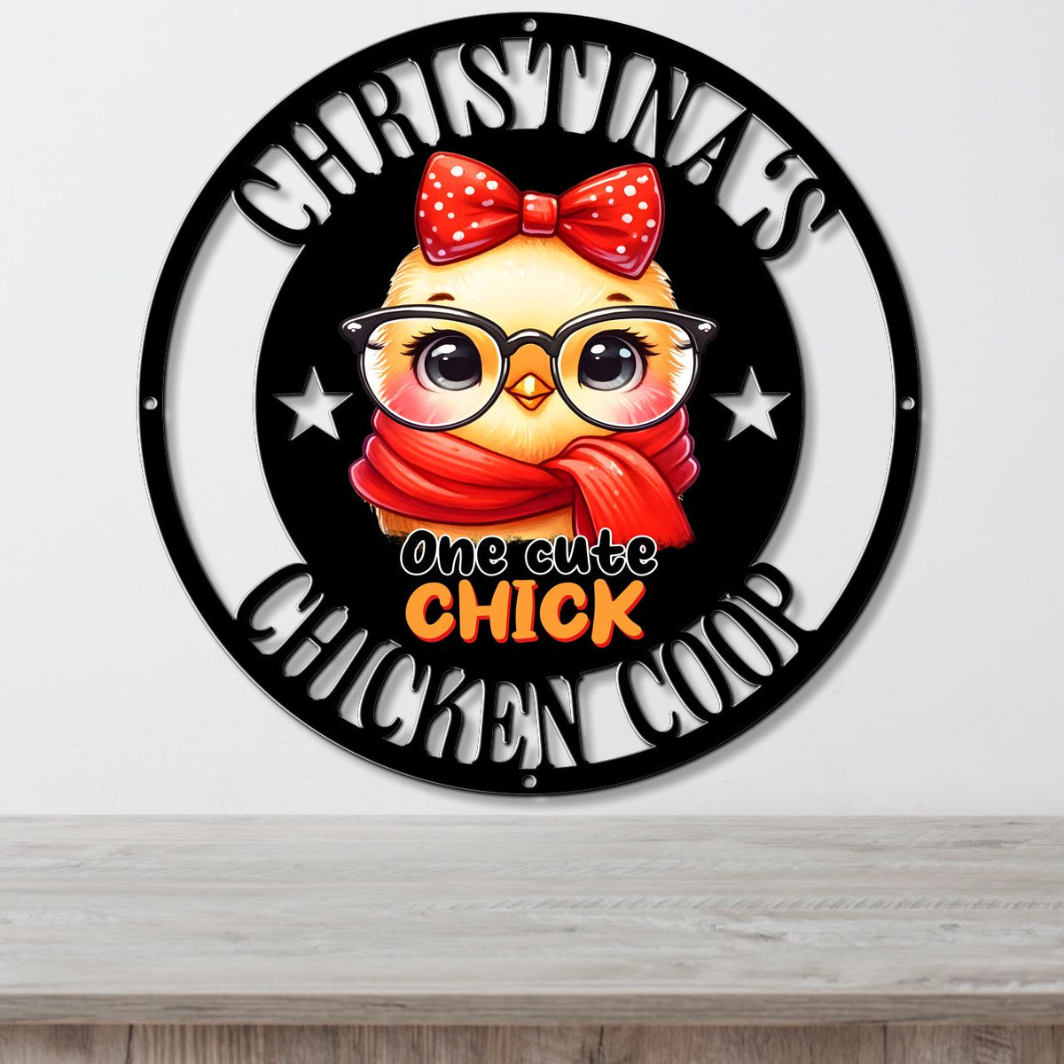 A circular black metal wall sign featuring a cartoon chick wearing a red polka-dot bow and red scarf, with the text 'CHRISTMAS CHICKEN COOP' and 'one cute CHICK' in white and orange lettering, shown hanging on a light gray wall above a wooden surface.