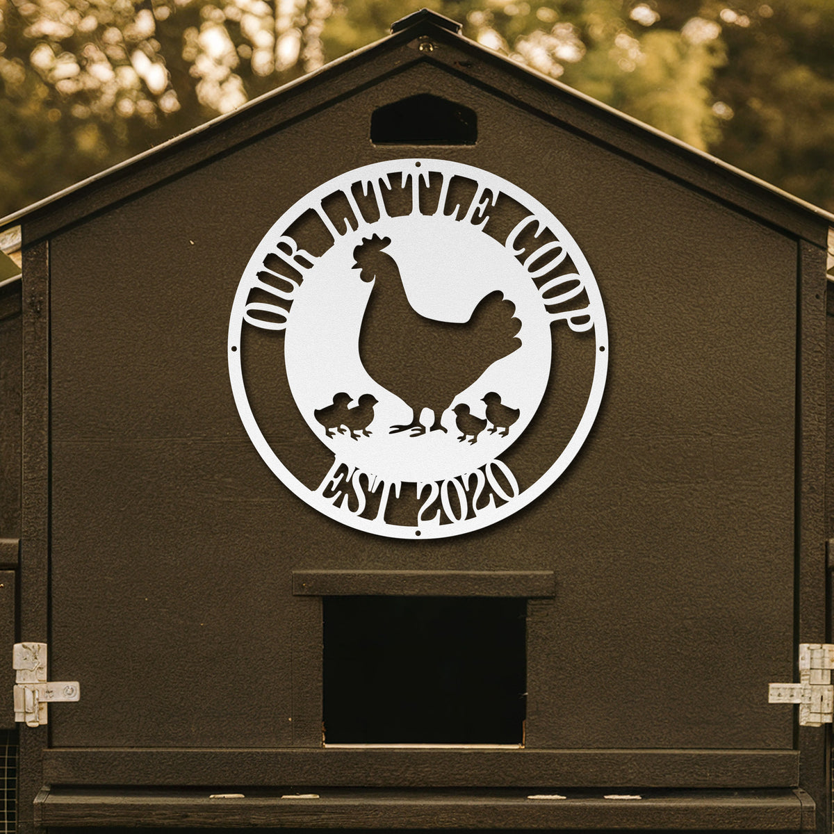 Brown chicken coop with a decorative metal plate featuring a rooster and chickens, set against a blurred natural background.