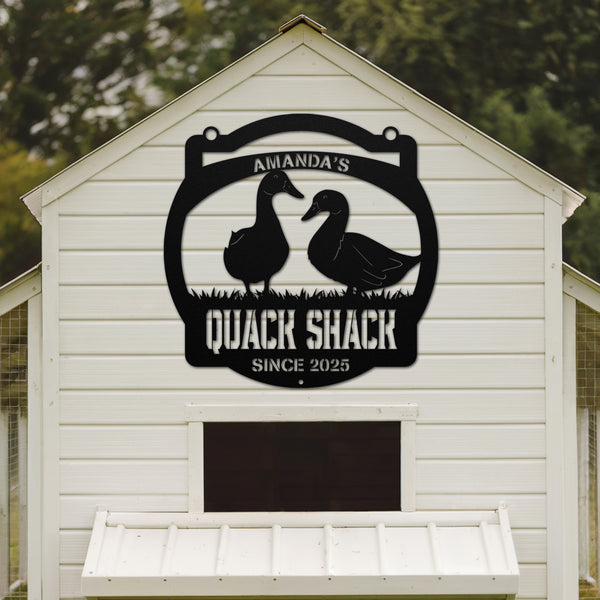 White shed with a black 'Quack Shack' sign featuring duck silhouettes on a wooden background.