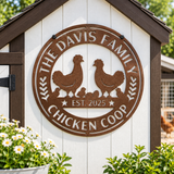 A round metal sign for a chicken coop mounted on a white wooden coop door. The sign is rusted brown with cutout silhouettes of two chickens, several chicks, and the text 'THE DAVIS FAMILY CHICKEN COOP' and 'EST.