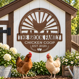 A decorative metal sign reading “The Brook Family Chicken Coop Est. 2020” mounted on a white and brown coop wall, with two chickens standing in front of the coop and flowers and a watering can around them.