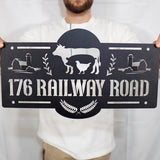 Person holding a decorative metal sign with farm-themed design and text '176 Railway Road'.