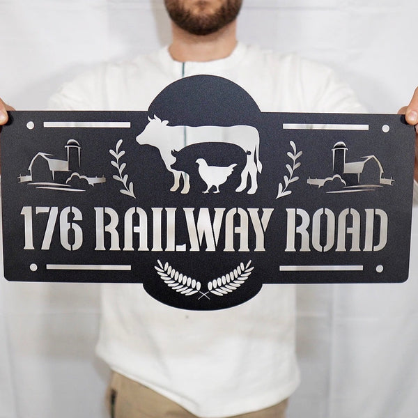 Person holding a decorative metal sign with farm-themed design and text '176 Railway Road'.